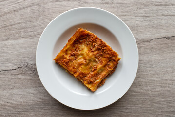 Italian meat Lasagne in a white dish on wooden background. Portion of traditional Lasagna on a plate. Top view