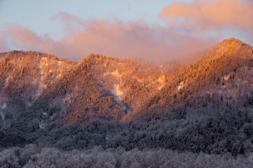 太陽の光にオレンジに色づけられた冬山。