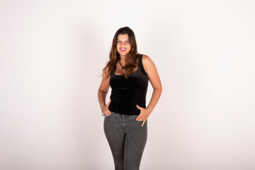 Portrait of a latin woman looking at the camera smiling with hands in pockets and positive attitude on pure background