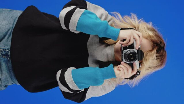 Vertical video, millennial woman looking through vintage camera viewfinder. Blue screen background
