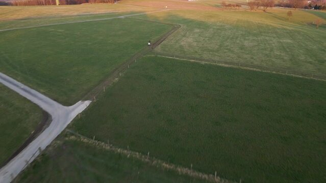Person sitting on his white scooter in a lush field during sunset. Wide angle aerial tracking shot revealing the true size of the landscape