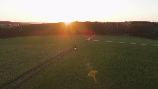 Person on a scooter standing within a green field during a magnificent sunset in Germany. Aerial establishing shot