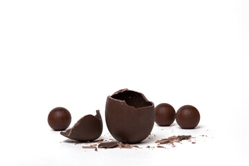 Cracked chocolate empty easter egg and chocolate round candies on white background. Chocolate treat for kids.