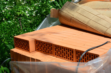 Red bricks on a pallet covered with polyethylene to protect from rain. A close-up of red face structural bricks.