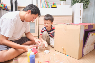 Asian father and son enjoy using paintbrush painting on cardboard box at home, Fun art and crafts...