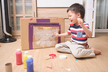 Cute Asian boy child enjoy using paintbrush painting on cardboard box at home, Fun art and crafts...