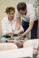 A couple in love in white shirts and jeans, a date in a pottery workshop, working together on one potter's wheel