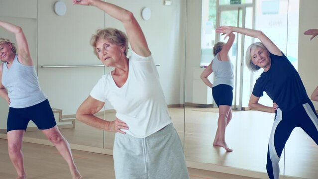 Portrait of cheerful senior woman enjoying active dancing during group training in dance studio