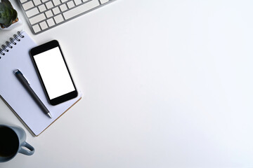 Top view mobile phone, notebook, coffee cup and wireless keyboard on white office desk.