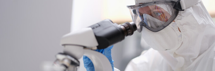 A specialist in uniform looks through a microscope, close-up