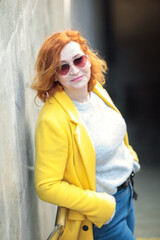 A young active woman with red hair, in bright clothes, a yellow coat and jeans