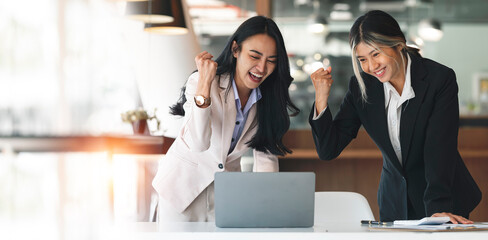 Two excited female executives celebrating success together at office.
