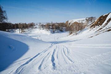 Fototapeta na wymiar Snowmobile tracks on white snow, the road passes through a snow-covered river, winter landscape, sunny weather clear sky, winter cold