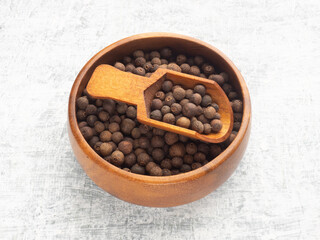 Fototapeta na wymiar Spice Allspice in wooden bowl and scoop on white concrete background. Macro. Healthy eating concept