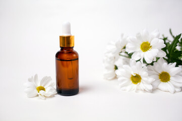 Fototapeta na wymiar A brown glass bottle with essential oil and a chamomile flowers. White background. Copy space. The concept of organic natural cosmetics