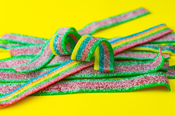 Rainbow stripes of sour jelly candies in sugar sprinkles on a yellow background. Top view. Colorful jelly candies in sugar sprinkles. Rainbow candy background. Selective focus. 