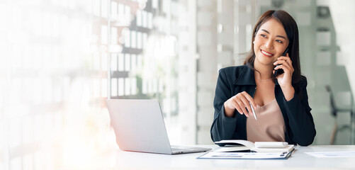 Portrait of beautiful smiling young entrepreneur businesswoman using smartphone and working on digital tablet in modern office room.