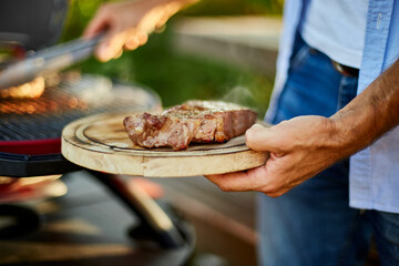 Man put down meat on a wooden board ready to eat grilled steak meat,