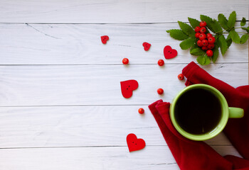 The red sweater is holding a green mug. Mug, rowan berries and hearts on a white wooden background. Flat lay composition with copy space.