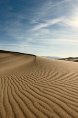 Deserted landscape. Sand dune with dark shadow on a background of blue sky.