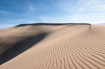 Deserted landscape. Sand dune with dark shadow on a background of blue sky.
