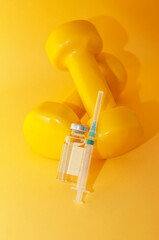 syringe and a jar of liquid lie on dumbbells on a yellow background, a vertical picture. the...