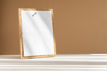 Mockup of blank sheet of white paper attached by button to cork board in rays of sunlight....
