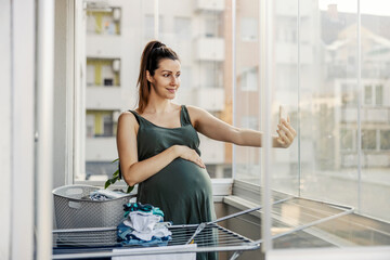 Pregnant woman poses and takes pictures on the phone while doing household chores. 
