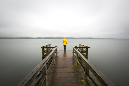 Germany, Schleswig-Holstein, Woman in yellow jacket standing on edge of lakeshore jetty