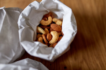 Top view cashew and  almond nuts on the table in a paper bag on wooden background, shopping grocery concept,  nuts delivary,  Zero Waste Food Shopping. Copy space..