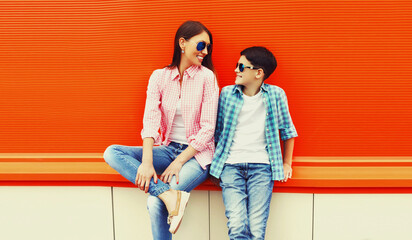 Portrait of mother with son teenager in sunglasses, checkered shirts on an orange background