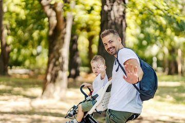 Happy father and son on a bicycle in nature waving.