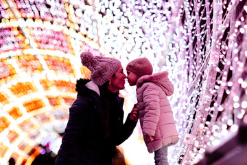 Mother embracing cute daughter by Christmas lights