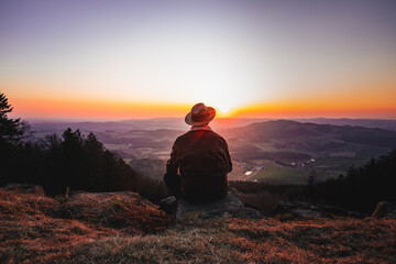 Man in a hat standing on top of a mountain as the sun sets in the Bavarian Forest, Germany.