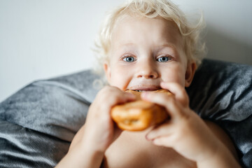 little girl with big blue eyes is biting a bun. portrait of a child, feeding and eating in pleasure.