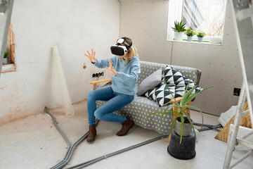 Woman gesturing with virtual reality simulator sitting on sofa in attic