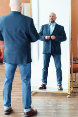 Portrait of confident handsome middle-aged bald man businessman with gray beard buttoning up blue...