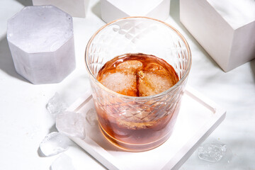 Strong alcohol drink glass. One glass of cognac or whiskey with ice cubes on white tile background with summer sunlight copy space