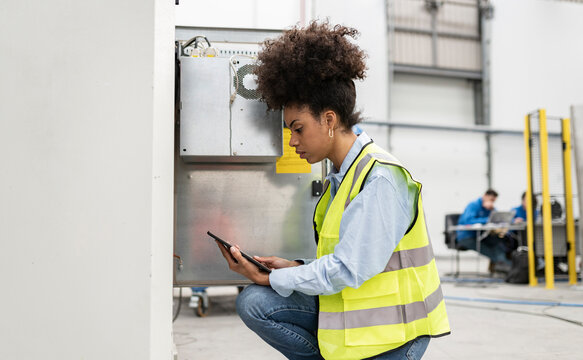 Technician using tablet PC crouching in factory