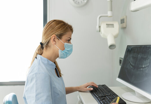 Dentist examining x-ray image through computer at dental clinic