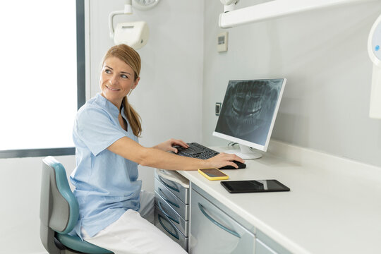 Dentist sitting on chair with computer on desk at dental clinic