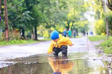 boy playing outdoors in puddles, autumn childhood rubber shoes raincoat yellow