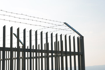 A tall iron fence with barbed wire against the sky. The birth of a prison or a dangerous facility. Border. - 495376217