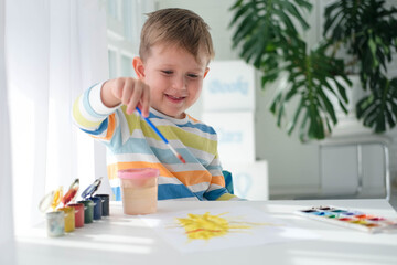 Happy kid painting with brush and colorful paints. A little boy draws a picture with paints on a...