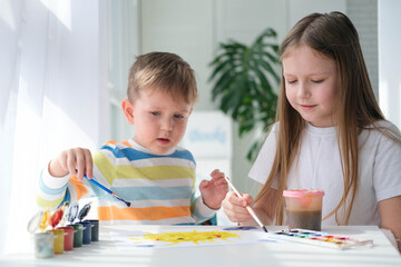 Brother and sister draw a picture with paints on a piece of paper. Children are learning to draw. Home creativity.