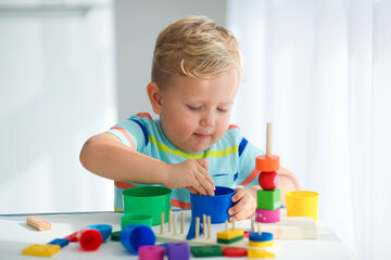 A little boy plays with wooden toys and builds a tower. Educational logic toys for children. Montessori games for child development. Children's wooden toy.