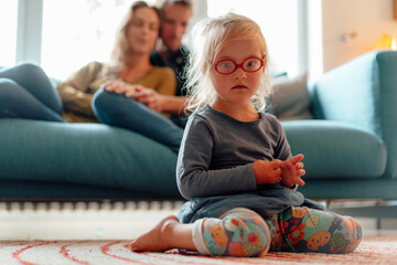 Cute little blond girl wearing eyeglasses sitting in living room at home