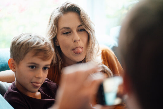 Blond woman with son sticking out tongue photographed by man at home