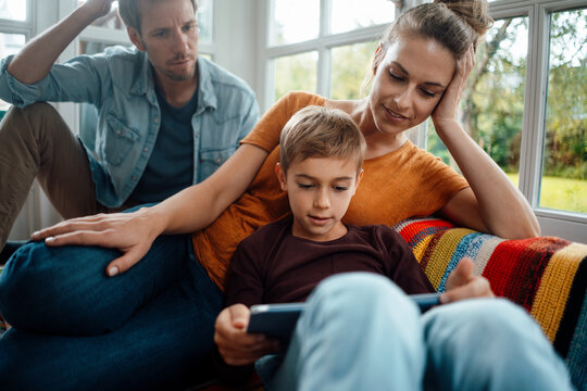 Man and woman looking at son using tablet PC sitting on sofa at home