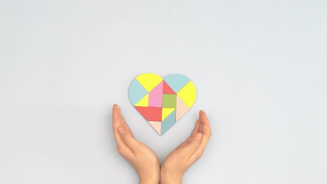 Child hands and colorful puzzle heart on light blue background. View from above. World autism awareness day concept